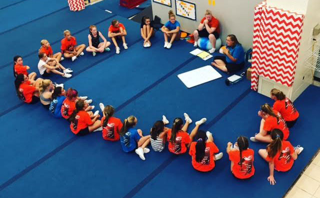 Athletes sitting in a circle on cheerleading mats